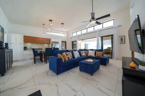 Ein geräumiges Wohnzimmer mit einem blauen Ecksofa, einem Essbereich und einer Küche im Hintergrund.