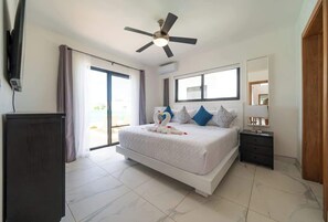 Un dormitorio con una cama, ventilador de techo, televisor, mesita de noche y puerta corredera.