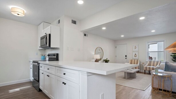 A modern kitchen with white cabinetry, a central island, and a dining area with striped chairs.