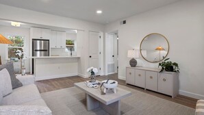 A modern living room with a sofa, coffee table, and a dining area with a kitchen in the background.