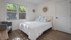 A bedroom with a bed, a chair, a window, a door, and a ceiling fan.