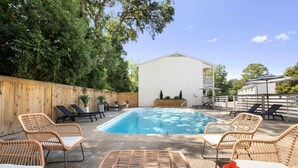 A backyard with a swimming pool, wicker chairs, and a white building.