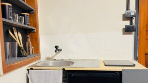 Une cuisine compacte comprenant un évier, un petit réfrigérateur et une étagère avec des ustensiles de cuisine.