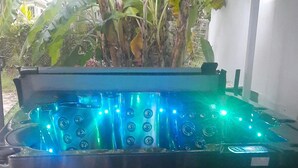 Un jacuzzi con múltiples chorros, rodeado por una zona cubierta con techo metálico y plantas en macetas.