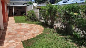 Un patio con un sendero de piedra, césped verde y un edificio con techo azul y paneles solares.