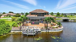 Een huis met een ruim terras met uitzicht op het water, een boot afgemeerd ervoor en een klein bruggetje naar een aangrenzend perceel.