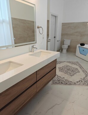 Un baño moderno con un espejo grande, dos lavamanos, un inodoro y una bañera.