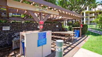A covered barbecue area with a grill, picnic tables, and a stone wall.