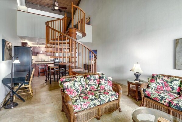 A spacious living area with a wooden spiral staircase, wicker furniture, and a dining area in the background. - Kamaole Sands (Kihei)