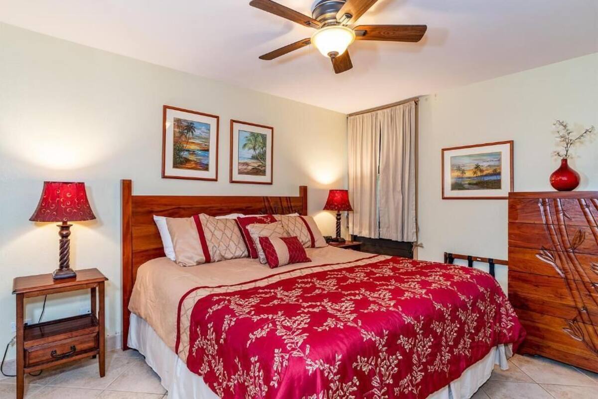 A bedroom with a wooden bed, red and beige bedding, two wall-mounted lamps, and framed pictures on the walls.