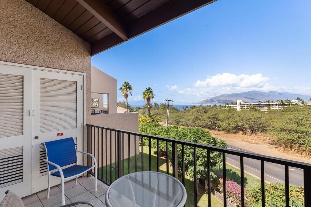 En balkon med udsigt til en vej, grønt og fjerne bjerge.