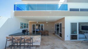A modern two-story house with a patio area featuring a barbecue grill, outdoor seating, and a large TV screen. - Ocean View • Style • Freedom (Casa Linda)