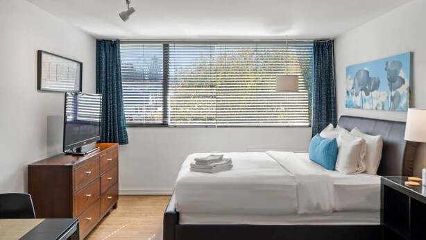 Una habitación de hotel con una cama, un escritorio, un tocador, una televisión y una ventana con persianas.
