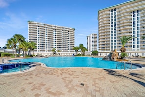 A swimming pool area with a clear blue pool, surrounded by a paved walkway, and adjacent to tall residential buildings. - St Maarten 1008, beachfront, sleeps 9, resort access (Destin)