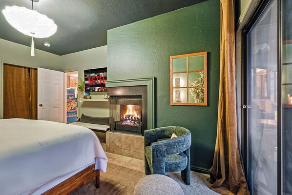 A bedroom with a bed, a fireplace, a TV, and a window with curtains.