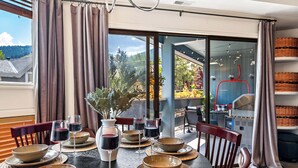 A dining area with a table set for four, including wine glasses and bowls, with a view of a garden and outdoor seating. - Après All Day! 3B Walk to Lifts Firepit, Poker, Ski Room, Disco Balls, Views! (Park City)