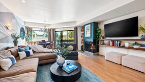 A modern living room with a sofa, coffee table, and ottomans. There is a fireplace, a TV, and a bookshelf. - Après All Day! 3B Walk to Lifts Firepit, Poker, Ski Room, Disco Balls, Views! (Park City)