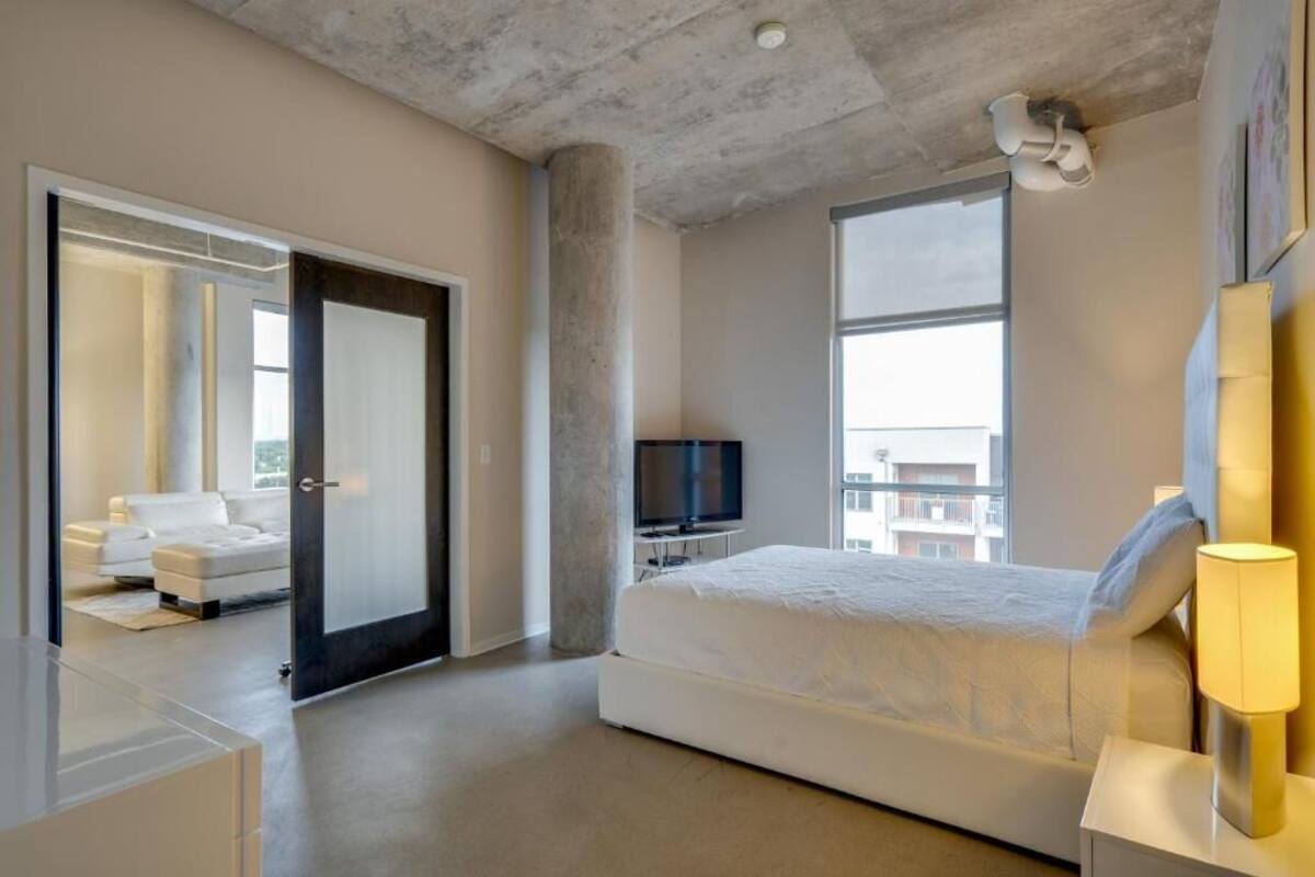 A modern hotel room with a large bed, a TV, and a view of the city.