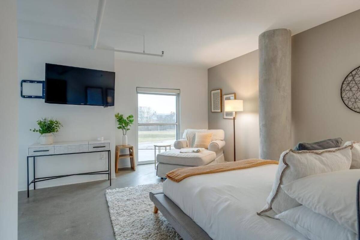 A modern bedroom with a large bed, a desk, a chair, and a TV mounted on the wall.