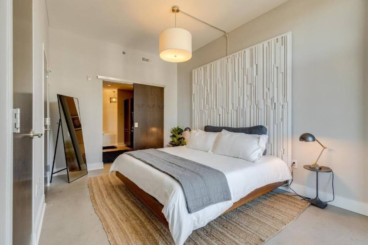 A modern bedroom with a large bed, a bedside table, a floor lamp, and a decorative wall panel.