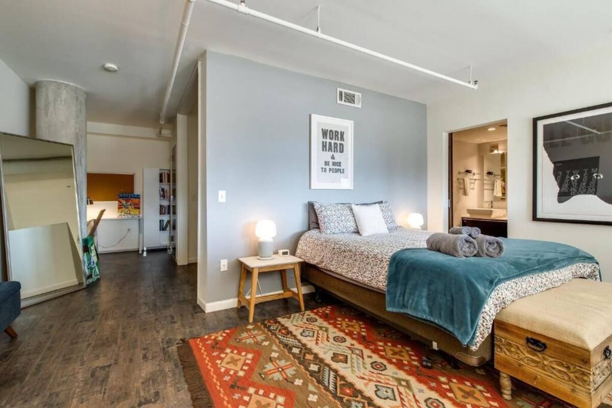 A modern bedroom with a bed, bedside tables, a rug, and a motivational poster on the wall.