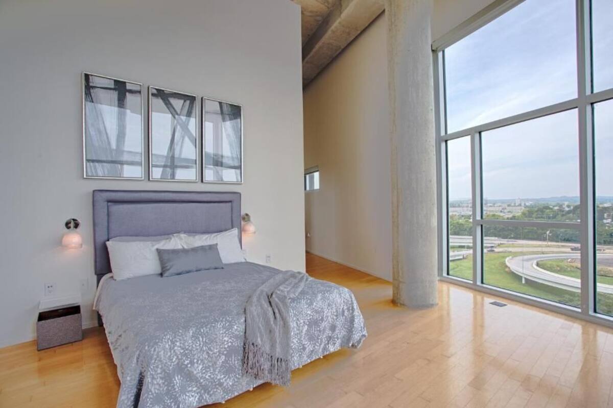 A modern bedroom with a large bed, a city view, and artwork on the wall.
