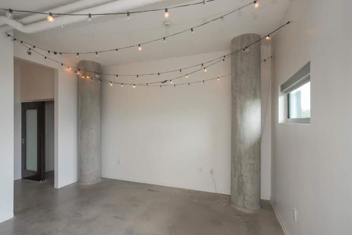A spacious room with concrete pillars, a visible door, and string lights on the ceiling.