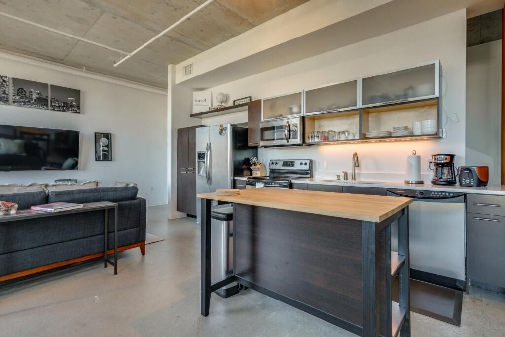 A modern kitchen with a central island, built-in appliances, and a dining area with a sofa and flat-screen TV.