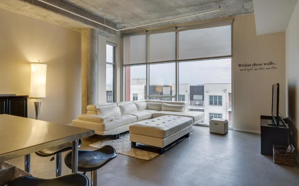 A modern living room with a large window, a sofa, a coffee table, and a lamp.