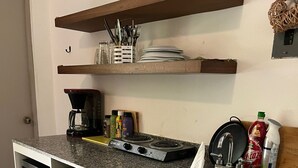 Una cocina compacta con lavavajillas incorporado, cafetera y fregadero. Hay estantes sobre la encimera con platos y utensilios.