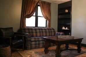A living room with a plaid sofa, a leather armchair, a wooden coffee table, and a bookshelf.