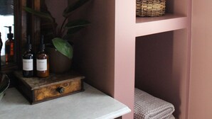 A bathroom with a wooden vanity, a mirror, a plant, and shelves with towels and toiletries. - Hickory House - South Park near UD Campus, Miami Valley Hospital, & Downtown (Dayton)
