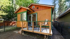 Una cabaña de madera con un porche, una puerta corrediza y un patio cercado.