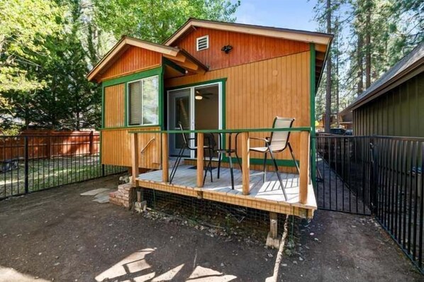 Una cabaña de madera con un porche, una puerta corrediza y un patio cercado.