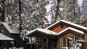 Una cabaña con un porche, rodeada de árboles cubiertos de nieve.