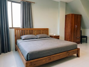 A bedroom with a wooden bed, a wardrobe, a nightstand, and a window with curtains. - Orient Hotel (Pattaya)