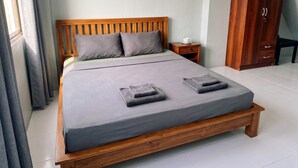 A neatly made bed with a wooden frame and grey bedding, a bedside table with a cup, and a wardrobe in the background. - Orient Hotel (Pattaya)