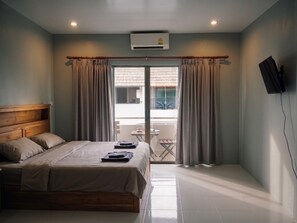 Ein Hotelzimmer mit Bett, Wand-Fernseher und einem Balkon mit Vorhängen.