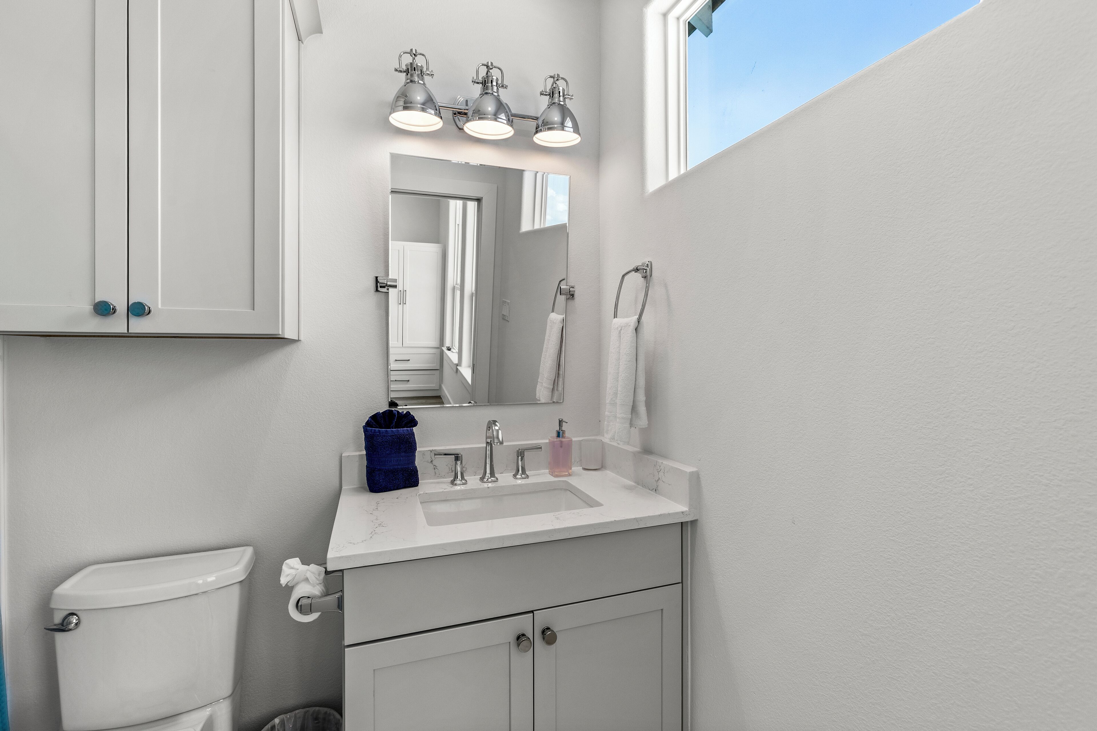 Une salle de bain avec des toilettes, un lavabo et un miroir. Il y a trois lampes au-dessus du miroir et une serviette accrochée au mur.