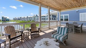 En træterrasse med udendørs møbler, udsigt til en sø og række huse i baggrunden.