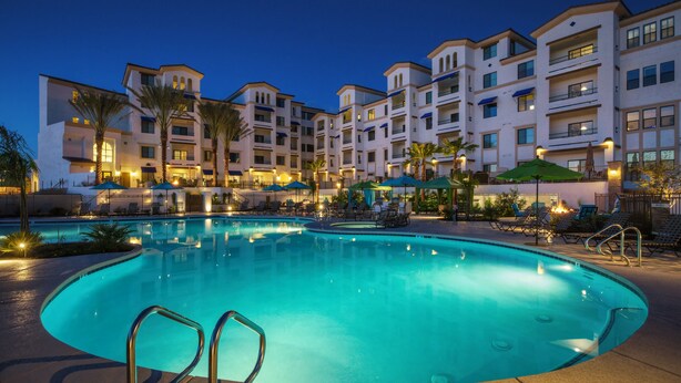 A swimming pool with lounge chairs and umbrellas, surrounded by a multi-story hotel building with balconies. - Queen Creek Vacation (Chandler)