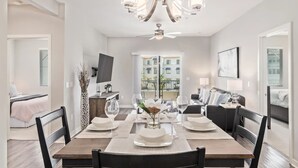 A dining area with a wooden table set for four, a chandelier, and a view of a building through the window. - Queen Creek Vacation (Chandler)