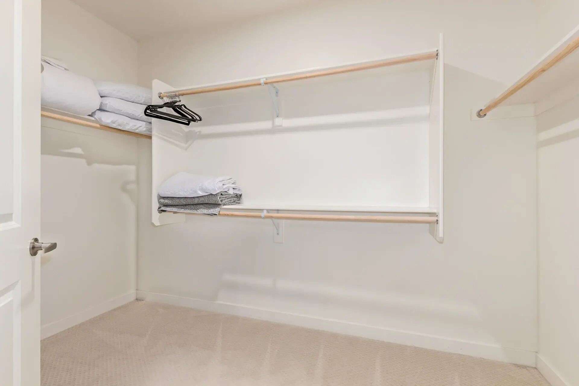 A walk-in closet with open shelves and hanging rods, featuring neatly folded towels and a black hanger.