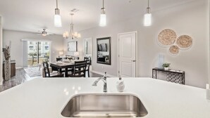 A modern kitchen with a central island, stainless steel sink, pendant lights, and a dining area with a table and chairs. - Queen Creek Vacation (Chandler)