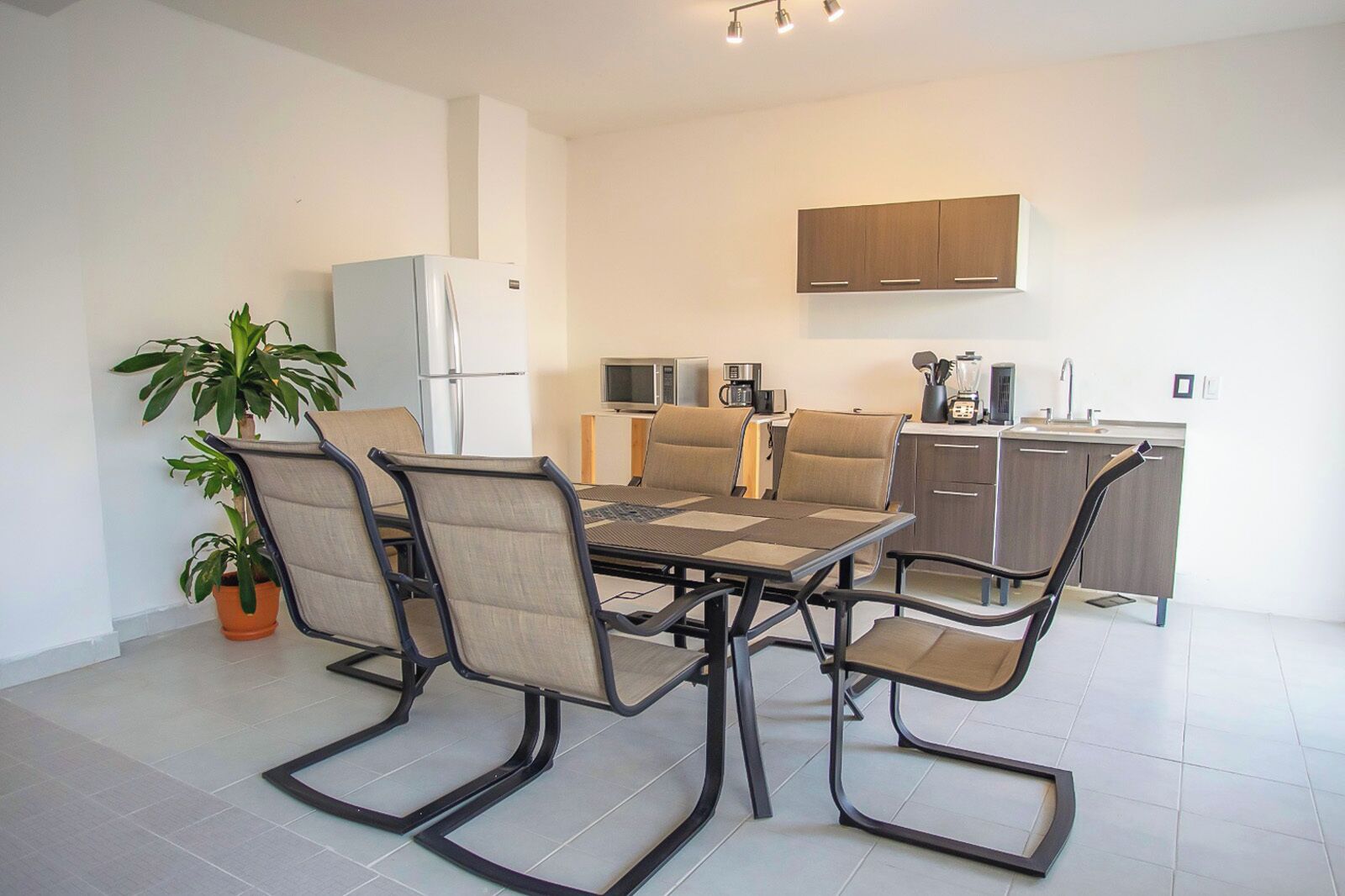 A modern kitchen with a dining area, including a table with chairs, a refrigerator, a microwave, and a sink.