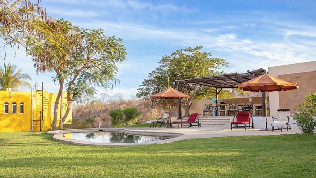 A pool area with lounge chairs and umbrellas, surrounded by a well-maintained lawn and trees. - Modern 2-Bedroom Condo with A/C in Stunning Los Cabos (MUNICIPIO LOS CABOS)