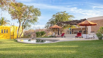 A pool area with lounge chairs and umbrellas, surrounded by a well-maintained lawn and trees.