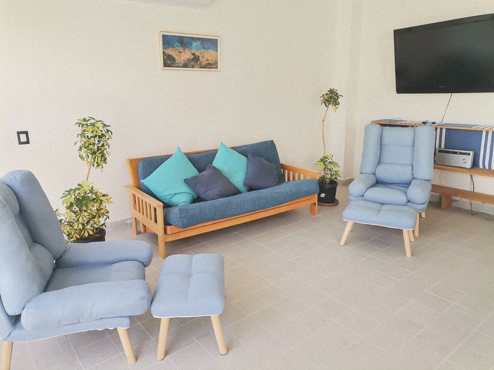 A living room with a sofa, two armchairs, a coffee table, and two potted plants.