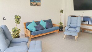 A living room with a sofa, two armchairs, a coffee table, and two potted plants. - Modern 2-Bedroom Condo with A/C in Stunning Los Cabos (MUNICIPIO LOS CABOS)
