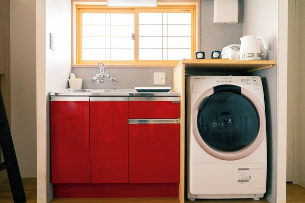 Una cocina compacta con armarios rojos, lavadora, cafetera y una ventana sobre el fregadero.